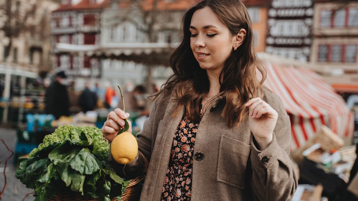 Young woman exploring Erfurt's vibrant farmers market, holding fresh produce in a bustling outdoor setting.
